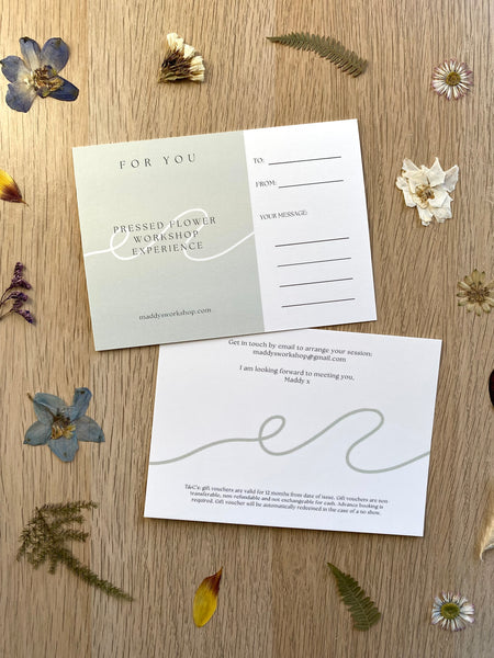 Two cards on a wooden surface with pressed flowers and leaves.