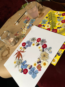 Table with floral pressed flowers on a sheet of paper, glasses, and a colorful placemat.
